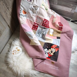 Könnte beinhalten: Eine rosa Patchwork-Babydecke mit verschiedenen gestickten Bildern von Tieren und Figuren, darunter Hasen, Bambi und Mickey und Minnie Mouse. Die Decke hat eine Waffelstruktur und enthält den Text "I mum".