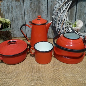 Könnte beinhalten: Ein Set aus vier roten Emaille-Küchenartikeln: eine Teekanne, eine Kaffeekanne, eine Tasse und ein kleiner Topf mit Deckel. Alle Artikel haben einen schwarzen Rand.