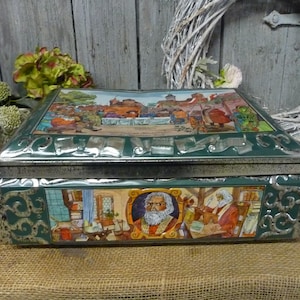 Könnte beinhalten: Eine grüne Vintage-Metallbox mit Scharnierdeckel. Der Deckel und die Seiten zeigen farbenfrohe Illustrationen von Menschen und Szenen. Die Box hat eine silberne Zierleiste und steht auf einer Jutefläche. Dekorativ und sammelwürdig.
