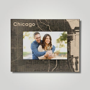 May include: A black and brown wooden picture frame with a map of Chicago, Illinois. The frame has a photo of a couple smiling and hugging. The text "Chicago" is printed on the frame.