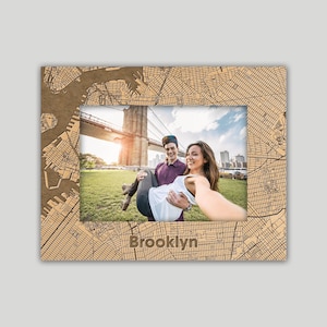 May include: A wooden picture frame with a map of Brooklyn etched into the frame. The frame holds a photo of a couple in front of the Brooklyn Bridge. The word "Brooklyn" is carved into the bottom of the frame.