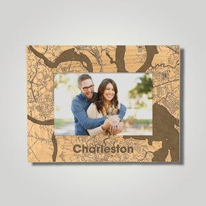 May include: A wooden picture frame with a map of Charleston, South Carolina, as the background. The frame has a cutout for a photo and the word "Charleston" is engraved below the cutout. A couple is pictured in the photo.