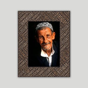 May include: A rectangular photo frame featuring a dark border with repeating text that reads 100th Birthday and Hundredth. The center displays a portrait of an elderly person with a white patterned cap, a white collared shirt, and a dark jacket.