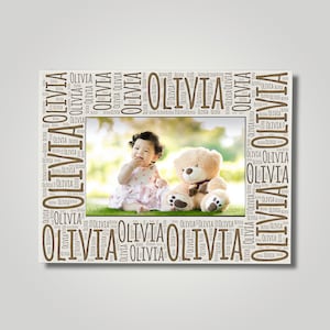 May include: A white frame with a brown word cloud of the name "Olivia" surrounding a photo of a young girl with a teddy bear. The photo shows the girl sitting on grass with the teddy bear beside her.