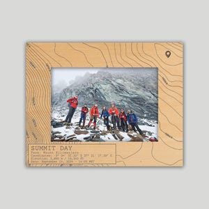 May include: A wooden photo frame with a topographic map design. The frame features a photo of a group of people standing on a mountaintop. The text "SUMMIT DAY" is printed on the frame, along with the peak name, coordinates, elevation, and date.