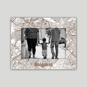 May include: A black and white photo of a family of three walking down a street. The photo is framed with a white frame with a brown map of Bulgaria printed on it. The text "Bulgaria" is printed in brown at the bottom of the frame.