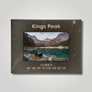 May include: A wooden photo frame with a topographic map design featuring Kings Peak, a mountain in Utah. The frame includes the peak's elevation of 13,528 feet and coordinates: 40° 46' 35" N 110° 22' 23" W.