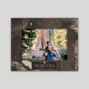 May include: A photo frame with a brown and gold topographic map design. The frame has a photo of a father and son in Sequoia National Park. The text "ESTD 1890 SEQUOIA NATIONAL PARK" is on the frame.