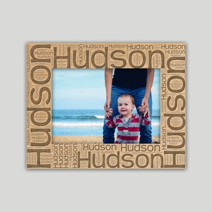 May include: A photo frame with a brown wood-like finish. The frame is made up of the word "Hudson" repeated many times. The photo inside shows a father and son walking on a beach.
