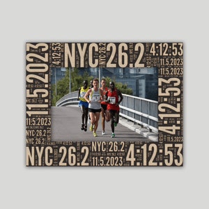 May include: A framed photograph featuring marathon runners in action. The frame is decorated with the text "NYC 26.2", "4:12:53", and "11.5.2023". The runners are on a bridge, with a cityscape in the background. The runners are wearing athletic gear.