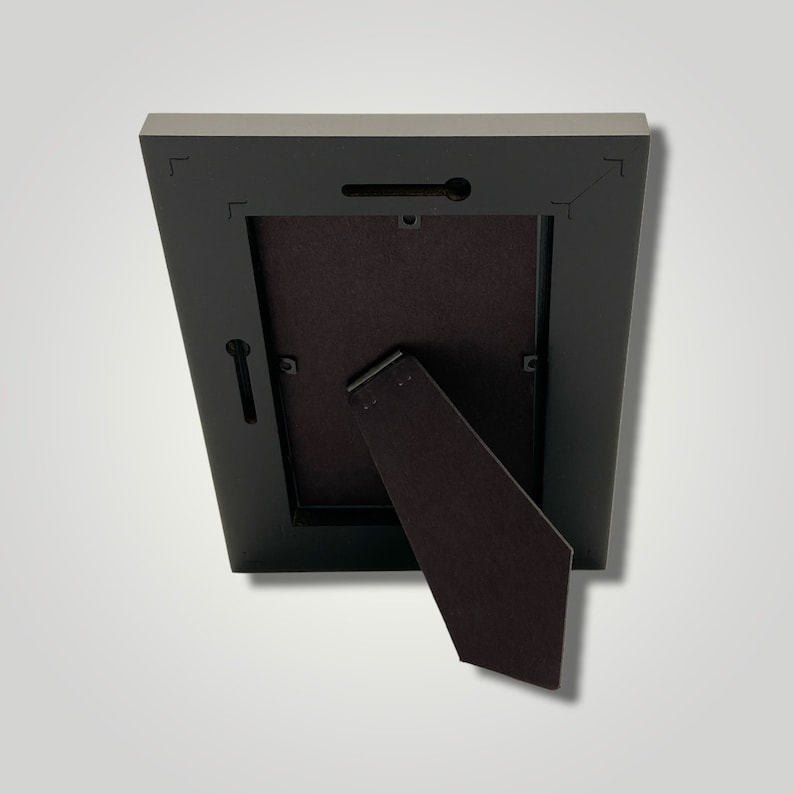 May include: Black picture frame with a brown cardboard backing and a fold-out easel stand on the back.