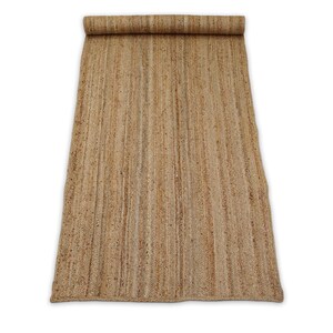 May include: A rectangular, rolled-up jute rug. The rug is a natural tan color with vertical woven lines. The top portion is rolled up, revealing the rug's texture. The rug is on a white background.