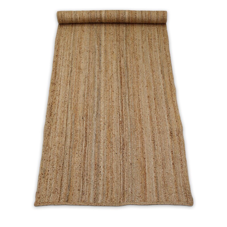 May include: A rectangular, rolled-up jute rug. The rug is a natural tan color with vertical woven lines. The top portion is rolled up, revealing the rug's texture. The rug is on a white background.