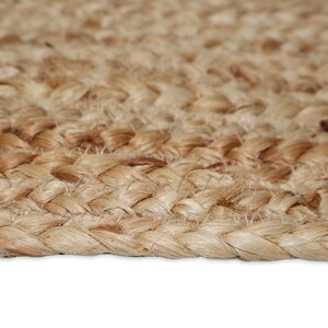May include: Close-up of a natural fiber rug with a braided texture. The rug is made of light brown and tan fibers, creating a warm, neutral color palette. The braided pattern adds visual interest and a rustic aesthetic.