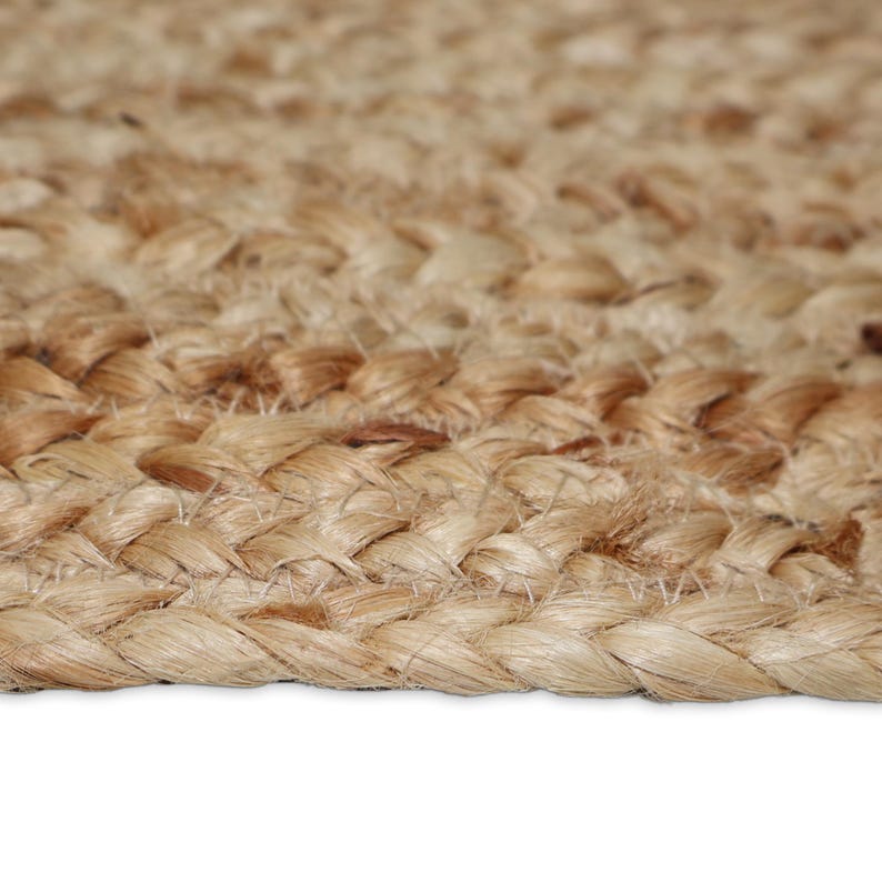 May include: Close-up of a natural fiber rug with a braided texture. The rug is made of light brown and tan fibers, creating a warm, neutral color palette. The braided pattern adds visual interest and a rustic aesthetic.