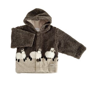 May include: A brown hooded jacket with a sheep design. The jacket has a soft, textured appearance and features three white sheep appliqués along the bottom. The jacket has a button closure and long sleeves. The hood is lined with a lighter color fabric.