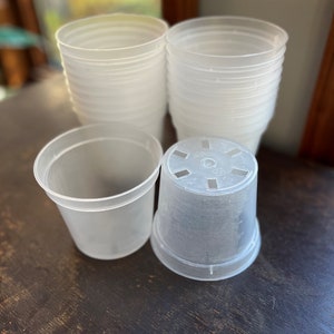 May include: A set of clear plastic plant pots, some stacked and some separate. The pots are all the same size and shape, and they have a smooth, translucent finish.