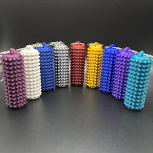 May include: A selection of colourful, cylindrical keychains. Each keychain is a different colour, including purple, white, blue, silver, red, gold, and teal. The keychains have a textured, spiky surface and are attached to silver keyrings.
