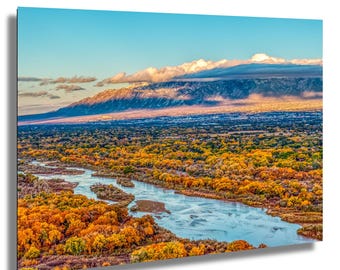May include: A panoramic view of a river winding through a valley with vibrant fall foliage. The river is a light blue color and the trees are a mix of yellow, orange, and red. In the distance, a mountain range is visible with a layer of clouds covering the peaks.