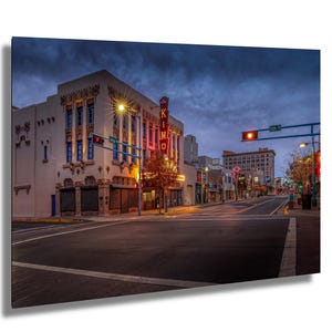 May include: A vintage brick building with a neon sign that reads "KIMO" in a dark blue sky. The building has a red tiled roof and a large, ornate facade. The street in front of the building is empty, and there are streetlights on either side of the road.