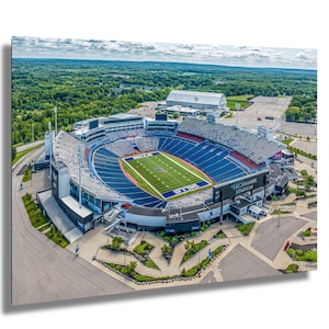 Puede incluir: Una vista aérea de un gran estadio de fútbol azul y blanco con un campo verde. El estadio está rodeado de un estacionamiento y árboles. Las palabras "HIGHMARK STADIUM" son visibles en un gran letrero.