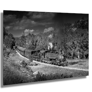 May include: Monochrome image of a steam train chugging through a woodland scene. The train, with its carriages, is on a track, emitting steam. The background features trees, grass, and a dramatic, cloudy sky.