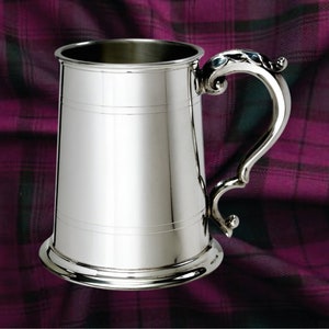 May include: A silver pewter tankard with a decorative handle. The tankard has a smooth, polished finish and a classic design.