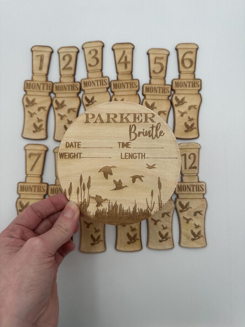 Puede incluir: Marcadores de hitos para beb&eacute;s de madera con un dise&ntilde;o de llamada de pato. Los marcadores est&aacute;n numerados del 1 al 12. Una placa redonda de madera separada con el texto "PARKER Brintle" y espacios para la fecha, el peso, la hora y la longitud.