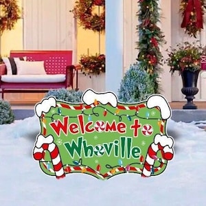 Może przedstawiać: Festiwalny znak świąteczny z napisem "Witamy w Whoville" w zielonych i czerwonych literach. Znak jest ozdobiony laskami cukrowymi, lampkami i czerwono-białym wirem miętowym.