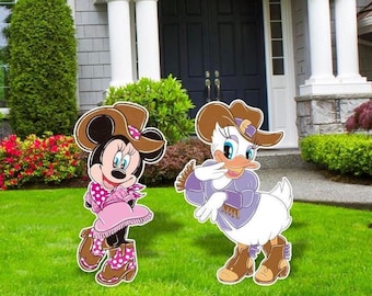 May include: Two cartoon yard decorations of Minnie Mouse and Daisy Duck in cowboy attire. Minnie Mouse wears a pink dress and boots, while Daisy Duck is in a purple outfit. Both characters have brown cowboy hats and boots, standing on a green lawn.