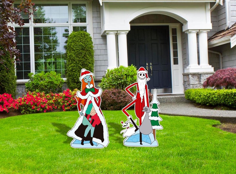 Może przedstawiać: Para dekoracji świątecznych do ogrodu przedstawiających Jacka Skellingtona i Sally z filmu Koszmar przed świętami. Jack jest przebrany za Świętego Mikołaja, a Sally ma na sobie czerwoną i białą sukienkę z białym futerkiem. Oboje stoją na niebiesko-białej podstawie z lodu.