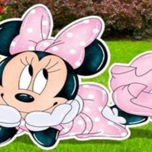 May include: A cartoon cutout of Minnie Mouse, featuring a pink and white polka-dot bow, dress, and shoes. Minnie Mouse is depicted with a tan face, black ears, and white gloves, resting her chin on her hands.