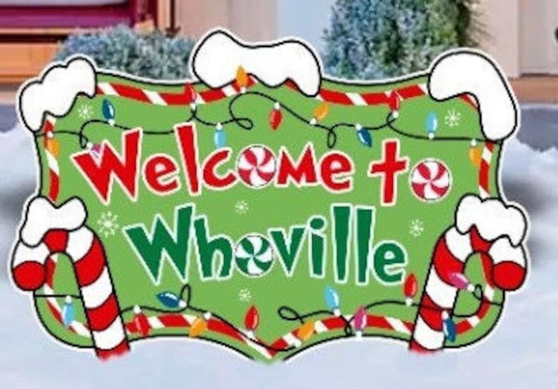Może przedstawiać: Zielono-czerwony znak świąteczny z napisem "Witamy w Whoville" otoczony cukierkami w kształcie laski i światełkami.