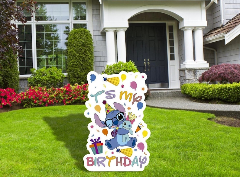 May include: A white cardboard sign with a blue cartoon character holding a stuffed animal. The sign says "It's my birthday" with colorful balloons and confetti around the character.