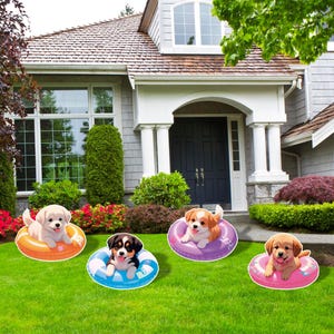 May include: Four puppy cutouts in colorful inflatable rings on a green lawn in front of a house. The puppies are a mix of breeds and colors, with the rings in orange, blue, purple, and pink.