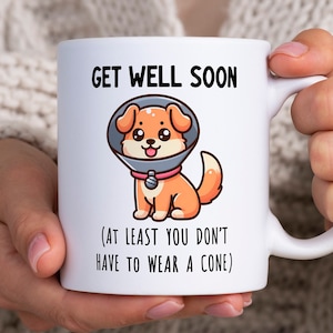 May include: White ceramic mug with a cartoon dog wearing a cone of shame. The mug reads "Get Well Soon (At Least You Don't Have To Wear A Cone)"