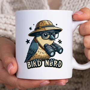 Könnte beinhalten: Weiße Keramik-Tasse mit einem Cartoon-Vogel-Design. Der Vogel trägt eine Brille, einen Safarihut und hält ein Fernglas. Auf der Tasse steht der Text "BIRD NERD". Das Design umfasst Sterne um den Vogel.