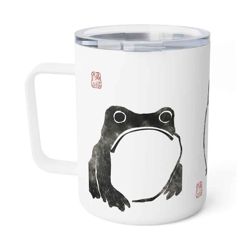 May include: White ceramic travel mug with a black and white ink illustration of a frog. The mug has a white handle and a clear lid.