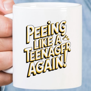 Può includere: Tazza da caffè in ceramica bianca con il testo "Peeing like a teenager again!" in lettere gialle e nere.