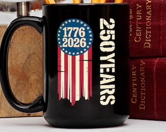 Könnte beinhalten: Schwarze Keramik-Tasse mit einem verblassten Design der amerikanischen Flagge. Die Tasse zeigt den Text "1776 2026" in einem blauen Kreis mit Sternen und die Worte "250 YEARS" in Weiß.