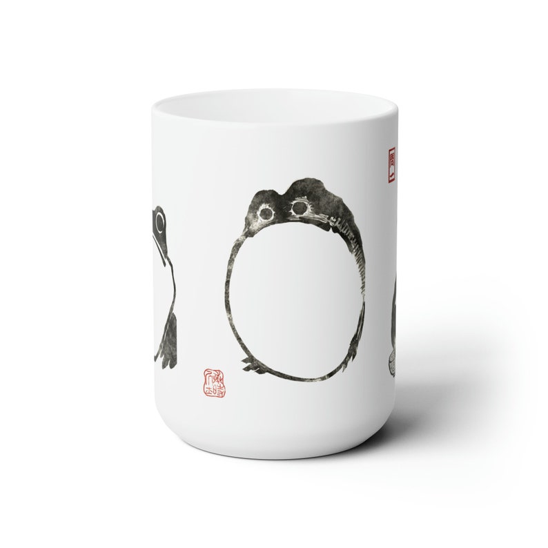 May include: White ceramic mug with black ink drawings of frogs. The frogs are in different poses, including one that is a circle. The mug has a red stamp on the side.
