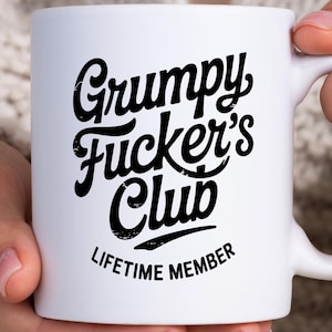 Op de afbeelding: Een witte keramische mok met zwarte tekst die Grumpy Fucker's Club leest in een gestileerd scriptlettertype, met de woorden LIFETIME MEMBER gedrukt in een kleiner, schreefloos lettertype direct onder de hoofdtekst op de voorzijde.