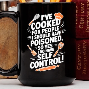 May include: Black ceramic mug with a white and orange graphic that reads "I'VE COOKED FOR PEOPLE I SHOULD HAVE POISONED, SO YES I DO HAVE SELF CONTROL!" The mug has a large black handle and is next to two red books.