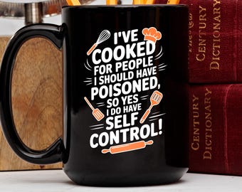 May include: Black ceramic mug with a white and orange graphic that reads "I'VE COOKED FOR PEOPLE I SHOULD HAVE POISONED, SO YES I DO HAVE SELF CONTROL!" The mug has a large black handle and is next to two red books.