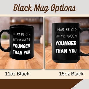 Puede incluir: Dos tazas de caf&eacute; negras con texto blanco. El texto en ambas tazas dice "I may be old but my knee is younger than you". La taza de la izquierda es una taza de 11 oz y la taza de la derecha es una taza de 15 oz.
