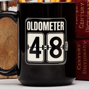 Könnte beinhalten: Ein Set aus drei Keramikbechern mit gesprenkelter, matter Oberfläche. Die Becher sind in Creme-, Hellgrau- und Dunkelgrautönen gehalten. Jeder Becher hat ein schlichtes, minimalistisches Design, ideal für Kaffee oder Tee.