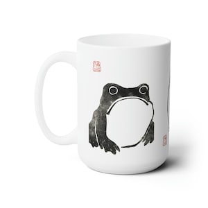 May include: White ceramic mug with a black and white illustration of a frog. The mug has a red stamp on the front and back.