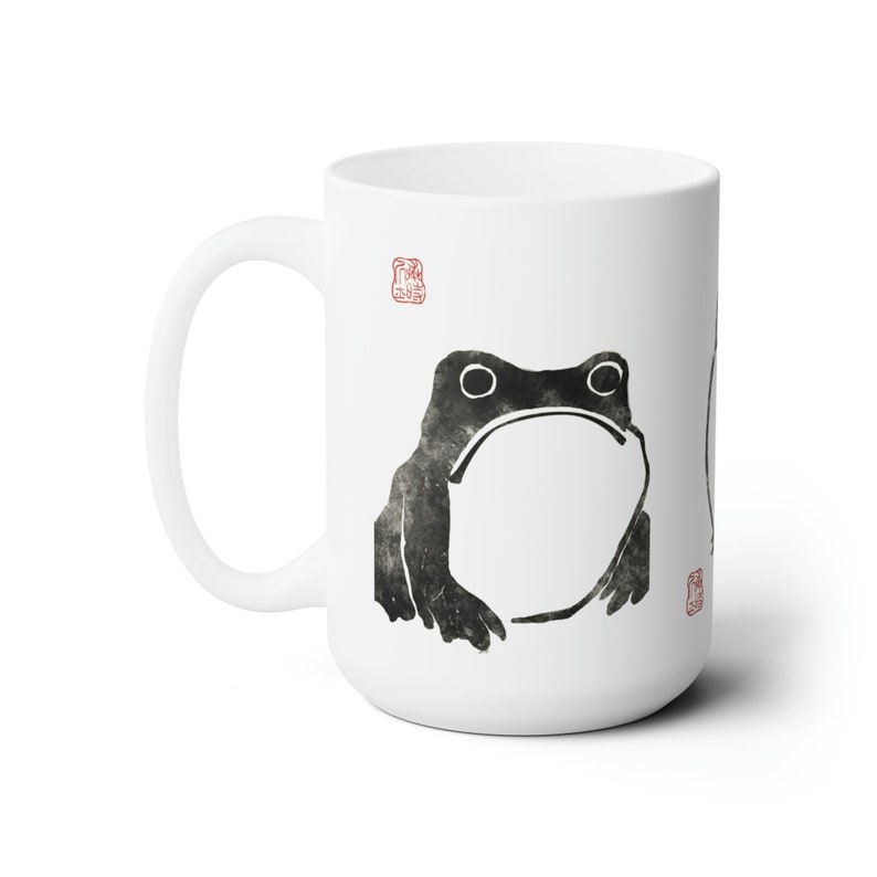 May include: White ceramic mug with a black and white illustration of a frog. The mug has a red stamp on the front and back.