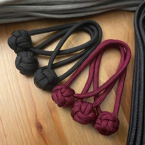 May include: Two black and two burgundy paracord keychains with knotted ends. The keychains are made of braided cord and have a decorative knot at the end.