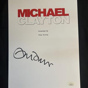 May include: A white script with the title "MICHAEL CLAYTON" in red letters. The text "Directed by Tony Gilroy" is below the title. The script is signed "Adam" in black ink.